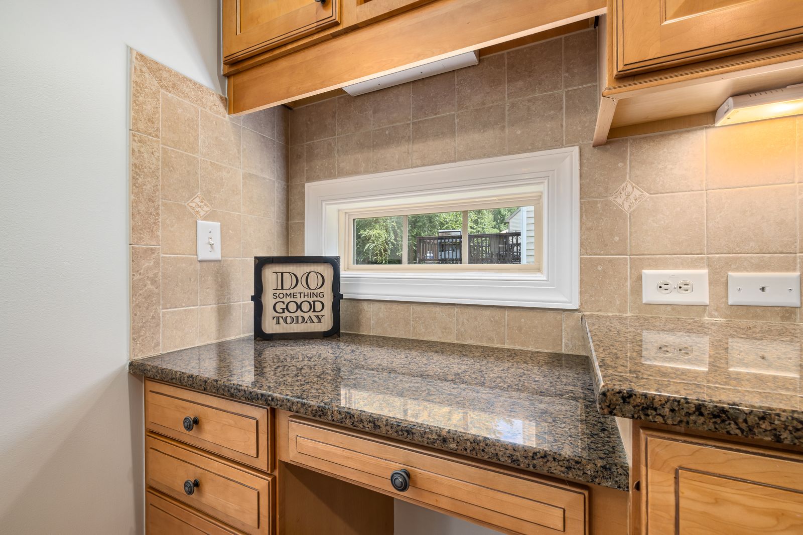 Clear stone kitchen counters beneath a window and warm wood cabinets